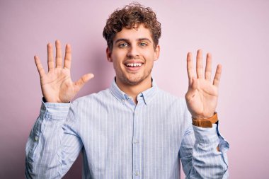 Sarışın, kıvırcık saçlı, beyaz arka planda çizgili gömlek giyen ve dokuz numaralı parmaklarıyla işaret eden genç, kendinden emin ve mutlu bir adam..