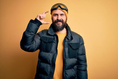 Sakallı, kar maskesi takan, kar maskesi takan, gülümseyen, kendine güvenen, el hareketi yapan, parmakları küçük gösteren ve kameraya bakan yakışıklı, kel bir kayakçı. Ölçü kavramı.