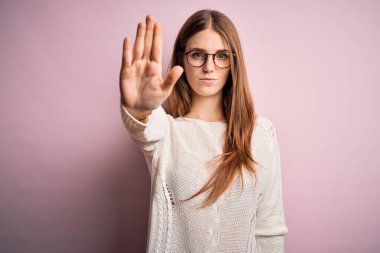 Genç, güzel, kızıl saçlı bir kadın pembe arka planda günlük süveter ve gözlük takıyor ve avuç içiyle şarkı söylemeyi kesiyor. Yüzünde olumsuz ve ciddi bir jest olan uyarı ifadesi.