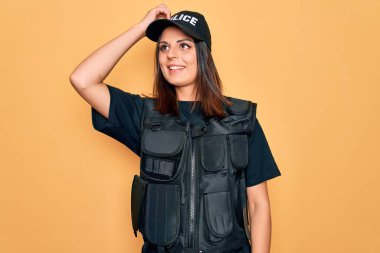 Genç, güzel esmer kadın polis üniforması giyiyor. Kurşun geçirmez ve şapka takıyor. Gülümsüyor.