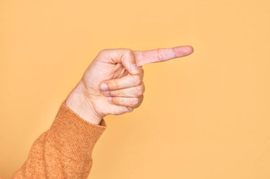 İzole edilmiş sarı arka plan üzerinde parmaklarını gösteren beyaz bir gencin eli işaret parmağıyla kenarı işaret ediyor ve bir seçim yapıyor.