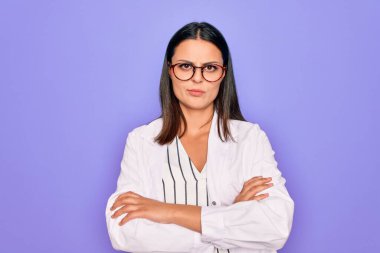 Paltosu ve gözlüğü mor arka planda kuşkucu ve gergin, yüzünde çapraz kollu tasvip etmeyen güzel esmer psikolog kadın. Negatif kişi.