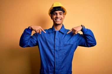 Mavi üniforma ve güvenlik kaskı takan, kendine güvenen, kendini gururlu ve mutlu gösteren genç, Afro-Amerikan işçisi..