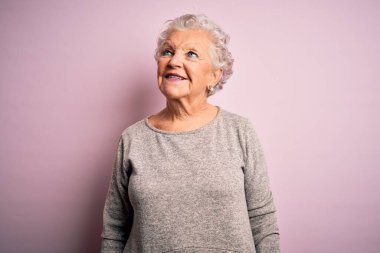 Son sınıftaki güzel bir kadın, günlük tişört giyip pembe arka planda dikiliyor. Gülümsüyor ve başka tarafa bakıyor..