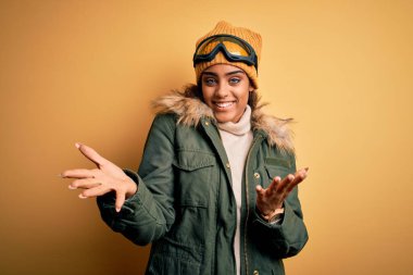 Genç Afrikalı Afro-Amerikan kayakçı kız kar sporu giyer ve kayak gözlüğü takar neşeli gülümseyerek el ele tutuşur ve kabul görür..