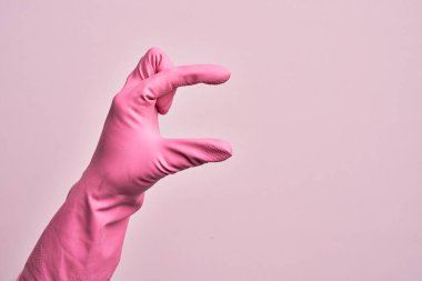 İzole edilmiş pembe arka plan üzerinde temizlik eldiveni olan beyaz bir adamın eli. Görünmez bir şeyi alıp, parmaklarında boşluk gösteren bir nesneyi tutuyor.