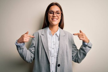 Beyaz arka planda ceket ve gözlük takan genç ve güzel esmer iş kadını. Yüzünde bir gülümsemeyle, gururlu ve mutlu bir şekilde kendini işaret ediyor..
