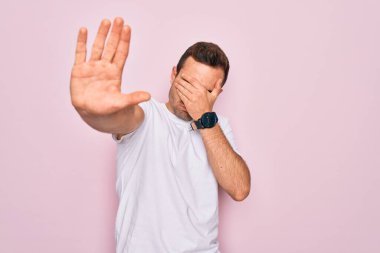 Mavi gözlü yakışıklı bir adam pembe arka planda dikilmiş pembe tişört giyiyor gözleri ellerle örtüyor ve üzgün ve korku ifadeleriyle jestleri durduruyor. Utanç verici ve olumsuz bir kavram..