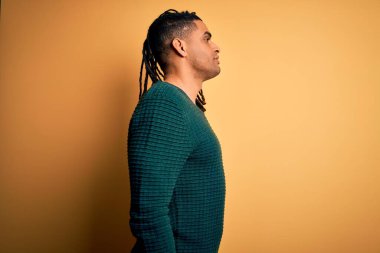 Rastalı yeşil süveter giyen Afro saçlı genç, yakışıklı Afro-Amerikan bir adam. Taraf arıyor, rahat poz veriyor, kendine güvenen bir gülümsemesi var..