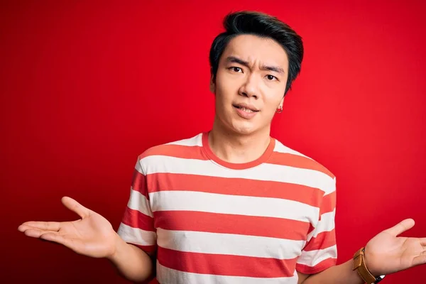若いですハンサムな中国人男性を身に着けているカジュアルな縞模様のTシャツ赤い背景の上に立って無謀と混同しないアイデアの概念 — ストック写真