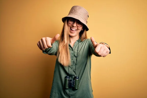 아름다운 금발의 탐험가가 모자와 안경을 쌍안경을 손으로 긍정적 행동을 승인하는 — 스톡 사진