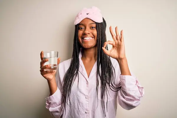 年轻的非洲裔美国女人 身穿睡衣 戴着眼罩 晚上喝着一杯水 手握手签 很好的象征 — 图库照片