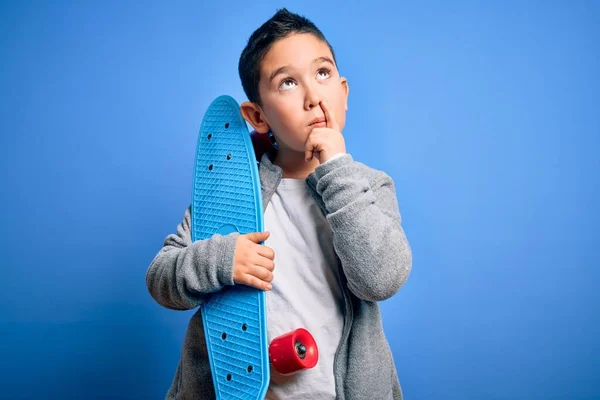 青い隔離された背景深刻な顔の上に近代的なスケートボードを保持する若い男の子のスケートボーダー質問について考えて 非常に混乱したアイデア — ストック写真