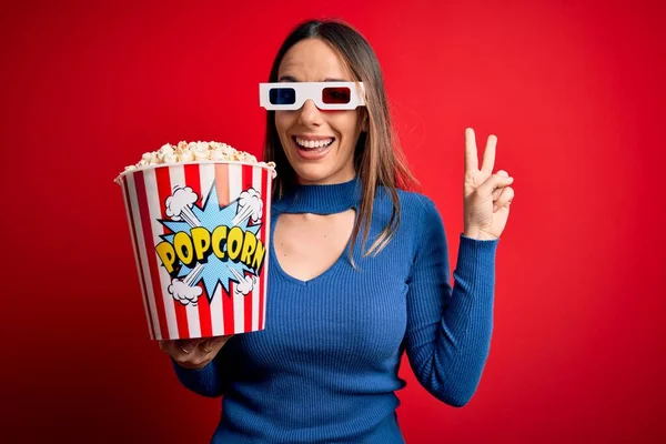 年轻的金发女郎戴着3D眼镜 吃着一包爆米花 看电影时微笑着看着摄像机 手指在做胜利的标志 第二点 — 图库照片