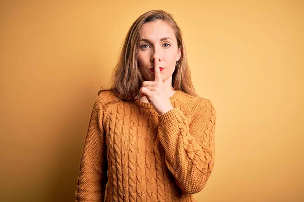 若い美しいブロンドの女性は 唇に指で静かになるように求めて黄色の背景に立ってカジュアルなセーターを着ています 沈黙と秘密の概念 — ストック写真