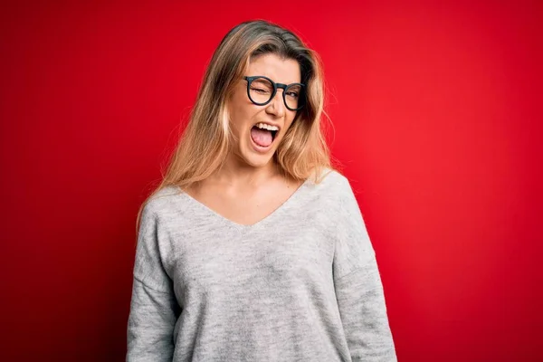 Jovem Mulher Loira Bonita Vestindo Suéter Óculos Sobre Fundo Vermelho — Fotografia de Stock