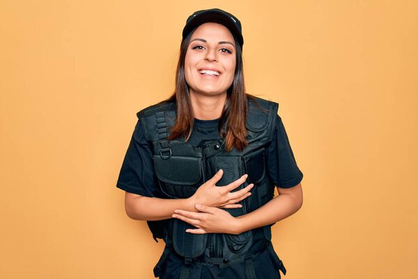 Young beautiful brunette policewoman wearing police uniform bulletproof and cap smiling and laughing hard out loud because funny crazy joke with hands on body.