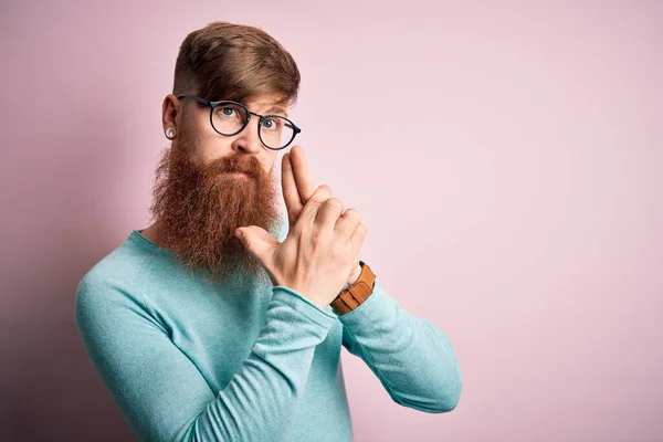 ハンサムなアイルランドの赤毛男で髭を生やして眼鏡をかけてピンクの隔離された背景手のジェスチャーで象徴的な銃を保持します シューティングゲームをプレイ 怒りの顔 — ストック写真