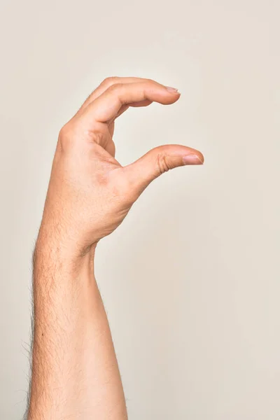 Hand of caucasian young man showing fingers over isolated white background picking and taking invisible thing, holding object with fingers showing space