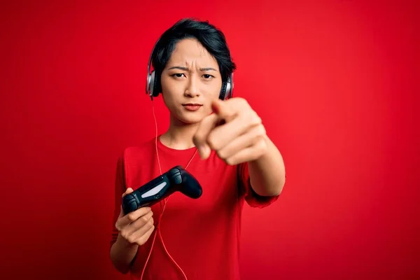 年轻美丽的亚裔游戏玩家女孩用操纵杆和耳机玩电子游戏 用手指指向相机和你 正面做出积极自信的手势 — 图库照片