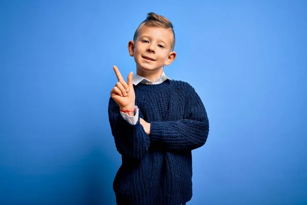 코카서스 아이가 스웨터를 웃으면서 손가락으로 카메라를 봅니다 — 스톡 사진
