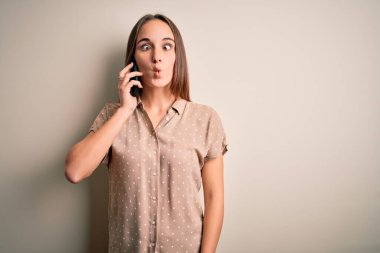 Genç ve güzel bir kadın, beyaz arka planda akıllı telefondan konuşuyor. Dudaklarıyla balık suratı yapıyor. Çılgınca ve komik bir jest. Komik ifade.