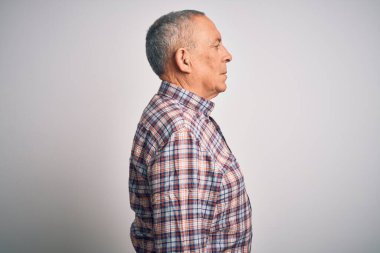 Üst düzey yakışıklı adam, günlük gömleğini giymiş, beyaz arka planda duruyor, yan tarafa bakıyor, rahat poz veriyor, kendine güvenen bir gülümsemesi var..