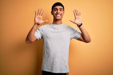 Yakışıklı Afro-Amerikan sporcusu spor giyer sarı arka plan üzerinde spor giyer ve parmaklarıyla on numarayı gösterirken kendinden emin ve mutlu gülümserdi..