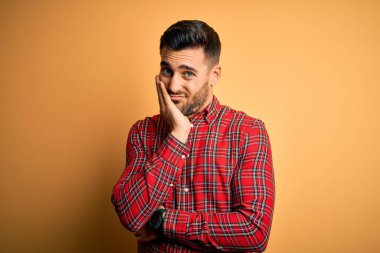 Genç yakışıklı adam izole sarı arka plan üzerinde duran rahat gömlek giyen yorgun görünümlü ve çapraz kolları ile depresyon sorunları ile sıkılmış düşünme.