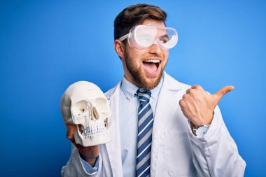 Sakallı, mavi gözlü, ceketli, gözlüklü, kafatasını tutan ve gülümseyen bir yüzü olan genç sarışın doktor.