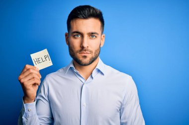 Genç aşırı çalışan iş adamı mavi arka planda kağıt tutarken yardım istiyor. Akıllı bir yüz ifadesiyle ciddi ciddi düşünüyor.