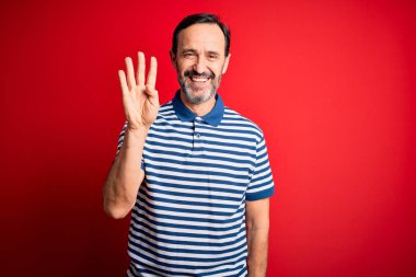 Orta yaşlı, beyaz çizgili polo giyen, izole edilmiş kırmızı arka planda duran ve dört numarayı işaret eden, kendinden emin ve mutlu gülümseyen bir adam..