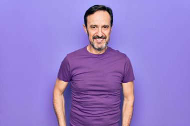 Orta yaşlı, mor tişört giyen yakışıklı bir adam izole arka planda mutlu ve havalı bir gülümsemeyle dikiliyor. Şanslı kişi..