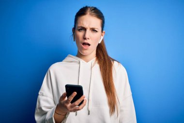 Genç kızıl saçlı sporcu kadın spor yapıyor kulaklık ve akıllı telefon kullanarak müzik dinliyor uykulu ve yorgun görünüyor, yorgunluktan yorgun ve akşamdan kalma, sabahları tembel gözler..