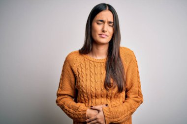 Genç, güzel esmer kadın, izole edilmiş beyaz arka plan üzerine günlük süveter giyiyor, midesi üstünde, çünkü hazımsızlık, acı verici bir hastalık, kendini iyi hissetmiyor. Ache kavramı.