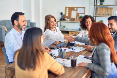 Bir grup iş adamı mutlu ve kendinden emin gülümsüyor. Birlikte çalışırken gülümseyerek ofiste el sıkışırken.