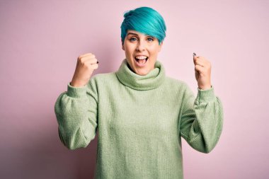 Mavi moda saçlı, balıkçı yaka kazak giyen genç ve güzel bir kadın kolları açık ve açık bir şekilde başarıyı kutluyor ve şaşırıyor. Kazanan konsept.