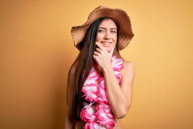 Tatilde mavi gözlü genç bir kadın bikini giyiyor ve Hawai leyleği kameraya kendinden emin bir şekilde bakıyor kollarını kavuşturup, çenesini kaldırarak gülümsüyor. Olumlu düşünüyorum..