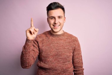 Pembe izole arka plan üzerine günlük kazak giyen yakışıklı beyaz bir adam başarılı bir fikir işaret ediyor. Heyecanlı ve mutlu. Bir numara..