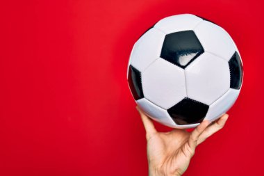 Güzel bir el futbol topunu izole edilmiş kırmızı arka planda tutuyor.