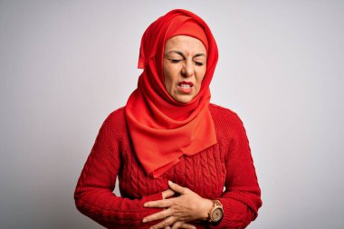 Orta yaşlı esmer kadın izole edilmiş beyaz arka plan üzerine geleneksel tesettür takıyor. Midenin üstünde el ele tutuşuyor. Çünkü hazımsızlık, acı veren bir hastalık, kendini iyi hissetmiyor. Ache kavramı.