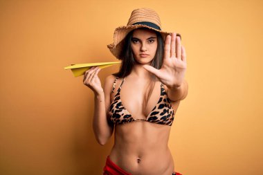 Bikini giyen, yaz şapkalı, elinde kağıt uçakla gezen genç ve güzel bir kadın dur işareti yapıyor. Ciddi ve kendinden emin bir ifadeyle savunma hareketi yapıyor.