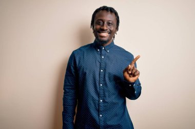 Genç, yakışıklı, Afro-Amerikan bir adam beyaz arka planda duran, yüzünde kocaman bir gülümsemeyle kameraya bakan, sıradan bir gömlek giyiyor..
