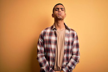 Sarı arka planda dikilen komik yüzlü, rahat gömlekli, yakışıklı Afro-Amerikan bir adam. Havayla şişmiş ağız, çılgın bir ifade..