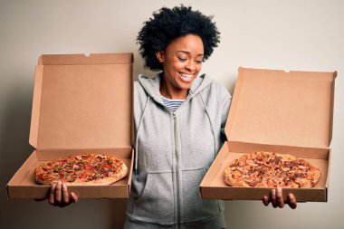 Genç, güzel afro-amerikan afro kadın mutlu ve güvenle gülümsüyor. Yüzünde tebessümle durarak kutular dolusu İtalyan taze pizzasıyla izole beyaz arka planda.