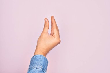 İzole edilmiş pembe arka plan üzerinde parmaklarını gösteren beyaz bir adamın eli. Görünmez bir şeyi alıp, parmaklarıyla uzayı gösteren bir nesneyi tutuyor.