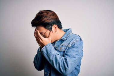 Beyaz arka planda kot ceket ve gözlük takan yakışıklı Çinli bir adam. Ağlarken yüzünü ellerle kapatan üzgün bir ifade. Depresyon kavramı.