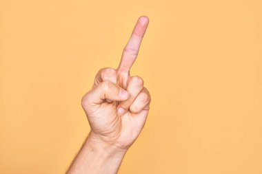 Hand of caucasian young man showing fingers over isolated yellow background showing provocative and rude gesture doing fuck you symbol with middle finger