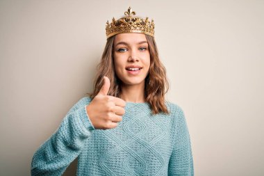 Soyutlanmış arka planda kraliçe tacını takan genç sarışın kız mutlu bir el hareketi yapıyor. Kameraya bakıp başarıyı gösteren ifade onaylanıyor.