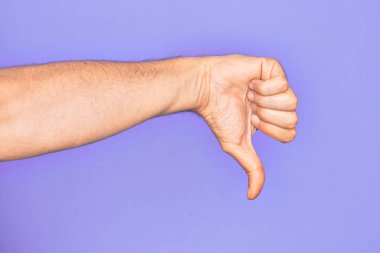 İzole edilmiş mor arka plan üzerinde parmaklarını gösteren beyaz bir gencin eli. Baş parmak reddetme hareketi, onaylanmama hareketi ve olumsuz işaret yapıyor.